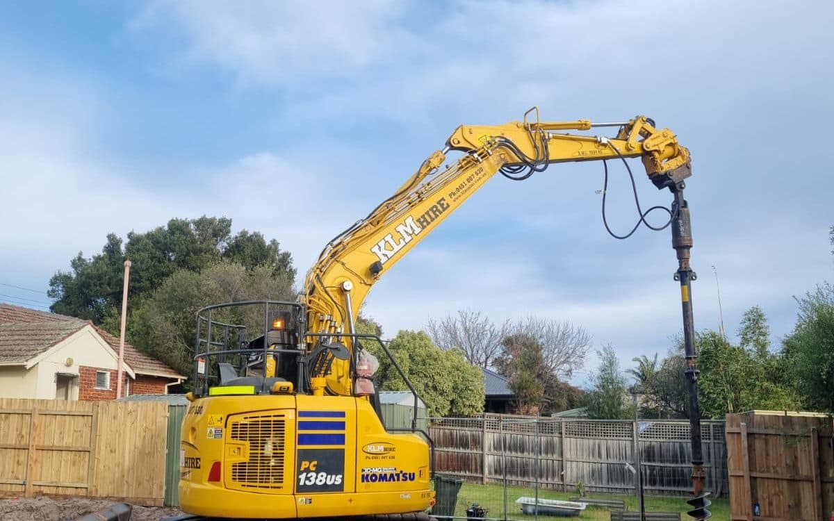 tracked excavator with an auger attachment drilling pier holes on a residential block