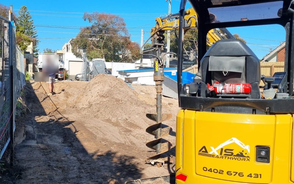 mini excavator with an auger drilling beside a pool on a residential block