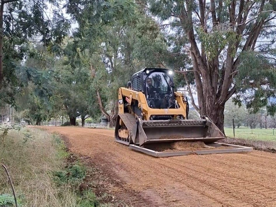tracked loader spreading crushed rock on a rural access driveway near mansfield