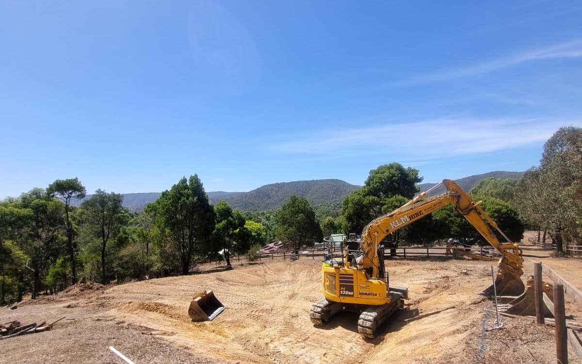excavator cutting a level pad on a rural block with the ranges behind