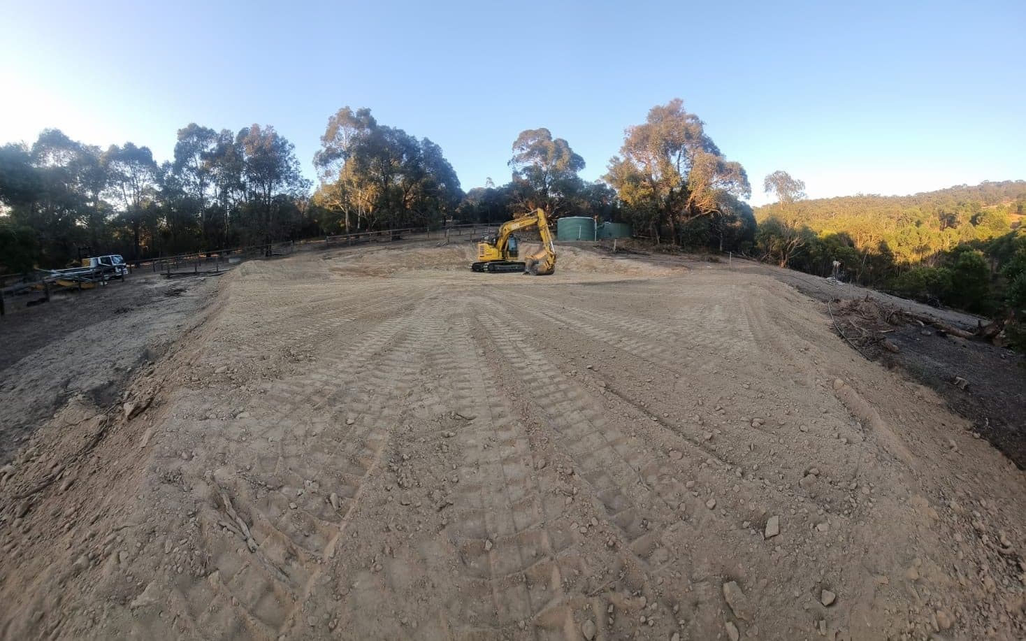 excavator cutting into a sloped block to form a building pad