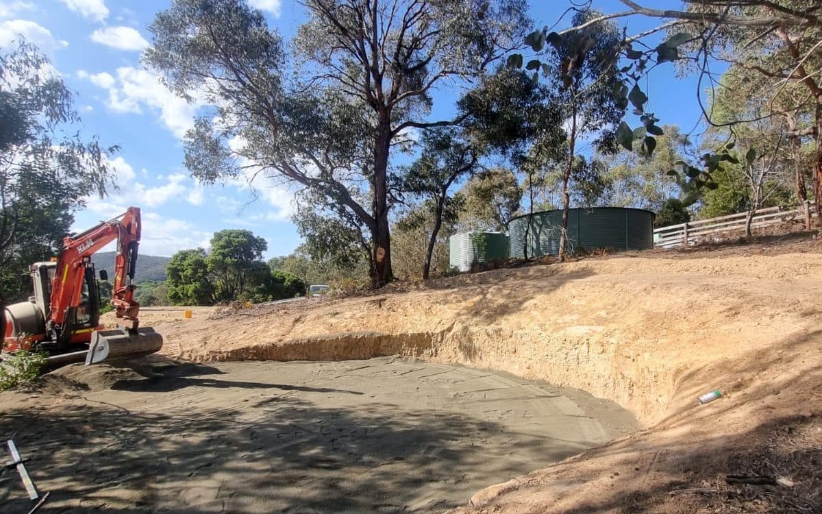 excavator beside a levelled pad cut into a sloped rural block, site cut, melbourne's north east