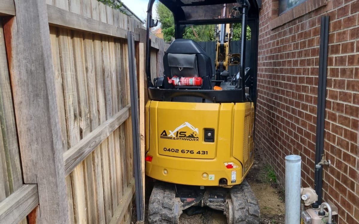 mini excavator in the narrow gap between a fence and a house wall
