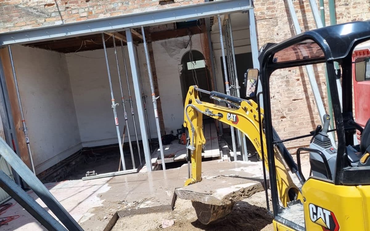 mini excavator working through narrow side access beside a house