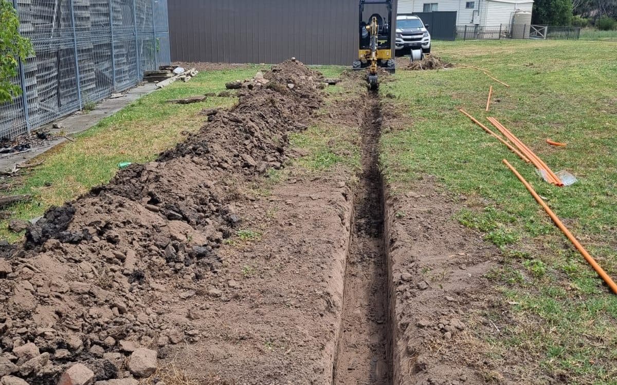 open service trench cut across a lawn with conduit ready to lay